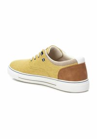 Zapatilla de lona amarilla con acentos de cuero marrón, suela de goma blanca y ojales de color claro. Presenta una superficie texturizada y detalles cosidos.