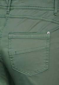 Pantalones de algodón verdes con un bolsillo cosido con un botón de metal visible y una costura decorativa a lo largo de las costuras, superficie texturizada.