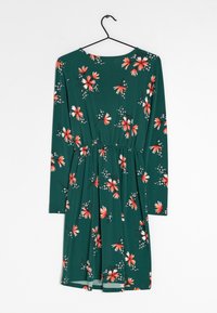 Šaty s dlouhým rukávem z zelené látky s květinovým potiskem červených a bílých květin, v pase stažené pro vytvoření nařaseného efektu.