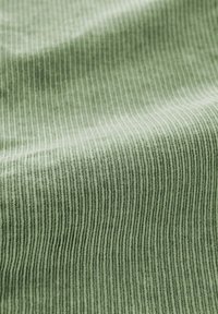 Groene ribstof met een zachte textuur, voorzien van verticale strepen en een subtiele glans, wat diepte creëert in het licht.