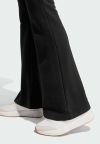 Černé rozšířené kalhoty z měkké látky, spárované s bílými teniskami s texturovaným svrškem a gumovou podrážkou, umístěné vedle sebe.