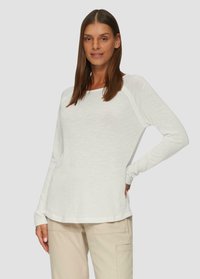 Chemise blanche à manches longues en tissu léger et texturé, avec une coupe décontractée et un col côtelé, associée à un pantalon cargo beige.