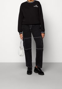 Czarna bluza z białymi wykończeniami, z logo na piersi, zestawiona z czarnymi spodniami cargo z kontrastowymi szwami. Dodatki obejmują małą białą torbę.