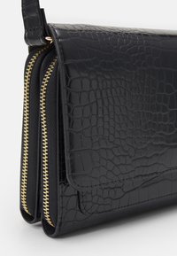 Černá kabelka s krokodýlí texturou a lesklým povrchem, s uzávěrem na zip, zlatými detaily a dvojitými přihrádkami.
