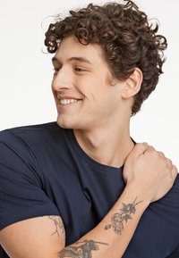 Navyblauwe t-shirt met korte mouwen, zachte textuur en een ronde hals. Kenmerkt een bloemtattoo op de onderarm en een lichte achtergrond.