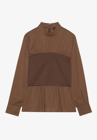 Braune Bluse mit langen Ärmeln und Stehkragen, gerafftem Stoff an Taille und Saum sowie einem kontrastierenden, strukturierten Mittelteil.