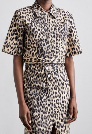 Femme portant une veste à manches courtes à boutons imprimée léopard et une jupe assortie taille haute avec fente avant et boutons.