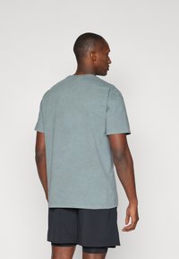 Kortærmet, falmet teal t-shirt i blødt bomuldsstof, med rund hals og afslappet pasform, parret med sorte atletikshorts.