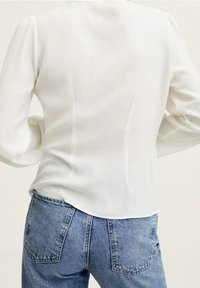 Hvid langærmet bluse med glat, letvægtsstof og afrundet kant, parret med højtaljede, lyseblå denimjeans med baglommer.