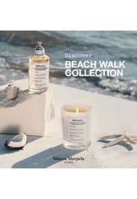 Świeca zapachowa i buteleczka perfum z kolekcji Beach Walk Maison Margiela na tle plaży, rozgwiazdy i kawałka kokosa.