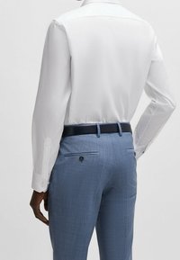 Witte lange mouwen shirt met een puntige kraag, gecombineerd met lichtblauwe textuurbroek met een slim fit en achterzakken. Donkerblauwe riem inbegrepen.