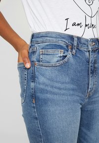 Modré džíny s vysokým pasem vyrobené z denimu, s předními kapsami, kontrastním šitím a mírně vybledlou texturou.