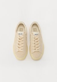 Sneakers beige con una toma in rete testurizzata e lacci in cotone. Presentano una suola in gomma e un'etichetta con logo sulla linguetta. Forma piatta e arrotondata.
