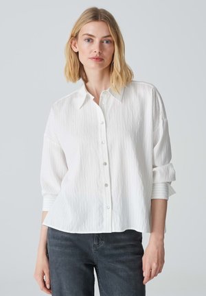 Witte button-up shirt met een textuurafwerking, met een klassiek kraag en opgerolde mouwen. Gecombineerd met grijze denim broek.