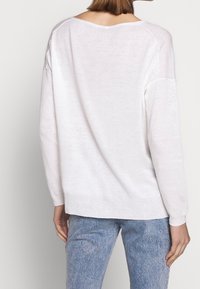 Weißer, leichter Strickpullover mit fallenden Schultern und geripptem Saum. Weiche Textur, leicht durchscheinender Stoff und lockere Passform.