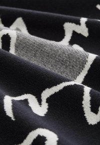 Falisty biały wzór na ciemnoniebieskiej, teksturowej tkaninie, ukazujący strukturę dzianiny z widocznymi detalami nici. Miękki i elastyczny materiał.