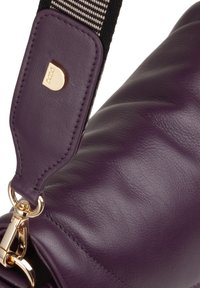 Purple leather bag corner with textured finish, featuring a gold hardware clasp and a striped fabric strap. Accentuated logo detail.