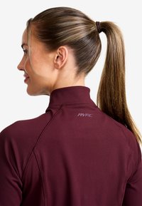 Bordeaux högkragad sporttopp med en slät textur och förstärkta sömmar, försedd med en liten "RVRC"-logotyp på baksidan nära halsringningen.