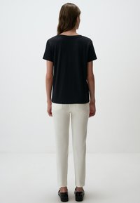 Czarna koszula z krótkim rękawem, luźny krój, zestawiona z kremowymi spodniami o dopasowanym kroju. Stylizacja dopełniona czarnym obuwiem.