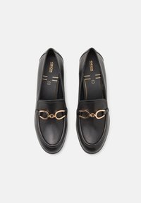 Mocassins en cuir noir avec un accent en métal doré à l'avant. Bout rond et texture lisse, conçus pour le confort.