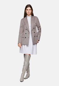 Gray double-breasted blazer with black buttons, worn over a white pleated dress and gray knee-high boots. Smooth texture and tailored fit.