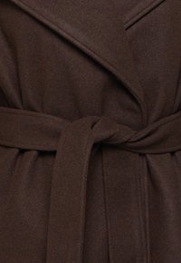 Gros plan d'un manteau en laine brun foncé noué à la taille avec une ceinture en tissu assorti et de larges revers.