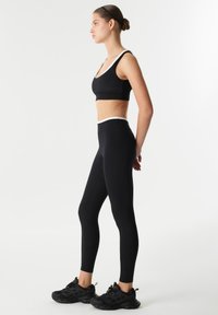 Black sports bra and leggings with white accents. Leggings feature a smooth texture and fitted design. Model wears black sneakers.