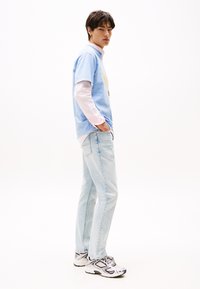 Lichtblauwe t-shirt met daaronder een roze lange mouwen shirt, gecombineerd met lichtblauwe jeans en zwart-witte sportieve sneakers.