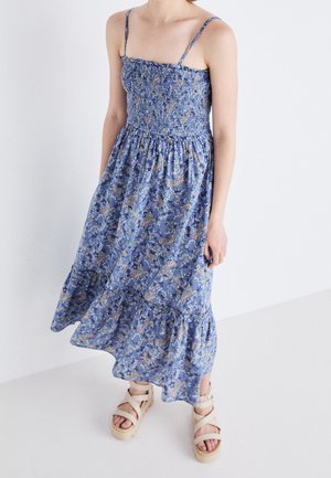 Robe maxi fleurie bleue avec un corsage smocké et des bretelles spaghetti ajustables, dotée d'un ourlet à volants et d'un tissu doux et léger.