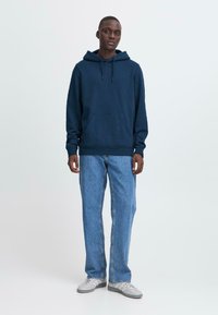 Felpa con cappuccio blu navy con tasca frontale, cappuccio con cordino, maniche lunghe. Abbinala a jeans dritti azzurri chiari e scarpe da ginnastica grigie.