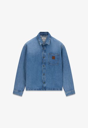 Camicia in denim blu a maniche lunghe con bottoni, colletto e taschino sul petto con una piccola toppa marrone.