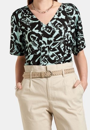 Vrouw draagt een zwarte en lichtblauw abstract patroon V-hals blouse, beige hoog getailleerde broek met een beige gestudeerde riem en een kettingketting.