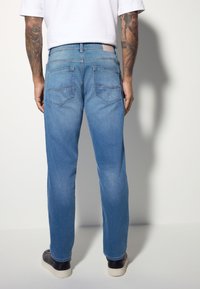 Jean en denim bleu clair à coupe droite, avec deux poches arrière, surpiqûres contrastées et une étiquette de ceinture texturée.