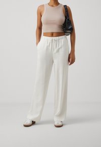 Lekki, biały materiałowy spodni o szerokich nogawkach z elastycznym pasem. Połączone z dopasowanym beżowym topem z krótkim rękawem oraz białymi trampkami z brązowymi akcentami.