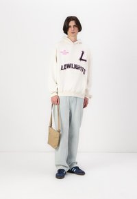 Felpa crema con stampe grafiche in rosa e blu navy, abbinata a pantaloni a gamba larga blu chiaro. Una borsa a tracolla beige e scarpe blu navy completano il look.