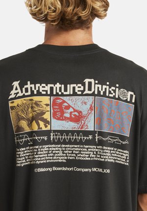 Black cotton t-shirt featuring a large multicolored graphic print on the back. Design includes illustrations of a lizard, butterfly, and abstract patterns, with text below.