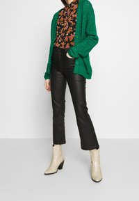 Grön stickad cardigan, blommig blus, svarta byxor i syntetläder och krämfärgade ankelstövlar i ormskinn med blockklackar. Texturerad och lager-på-lager-look.