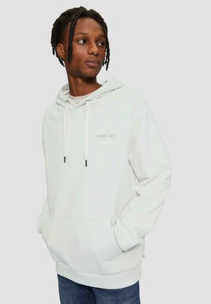 Witte hoodie met verstelbare trekkoorden en voorkantzak. Voorzien van "STREET ART" opdruk op de borst. Gladde stoftextuur. Gecombineerd met blauwe spijkerbroek.