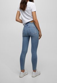 Jeans ajustados de denim de color azul claro, de cintura alta, con un acabado suave y dos bolsillos traseros. Combinados con una camiseta blanca de manga corta y zapatillas blancas.