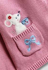Rosa stickad tyg med en broderad mus i en ficka, som håller en blå korg med röda blommor och en accentrosett i blå broderi.