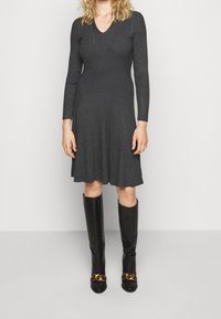 Abito a maglia a coste grigio scuro con scollo a V e maniche lunghe, gonna svasata. Abbinato a stivali neri al ginocchio con un'accenno di catena dorata.