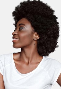 Kvinna med voluminöst, lockigt svart hår som bär en vit T-shirt. Hon har en silverdroppeörhänge med en triangulär svart accent.