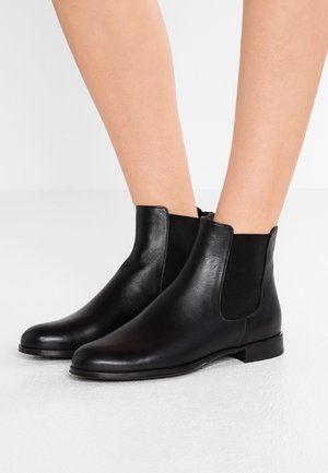 Zwarte leren enkelboots met elastische zijpanelen, een ronde neus en platte zool, met een gladde textuur en minimalistisch design.