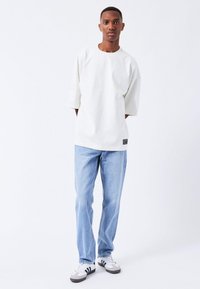 Witte oversized t-shirt met korte mouwen, gecombineerd met lichtblauwe rechte jeans. De schoenen hebben zwart-witte accenten.