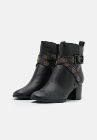 Bottines noires en cuir texturé, présentant une sangle décorative avec un motif de logo et un talon carré pour la stabilité.