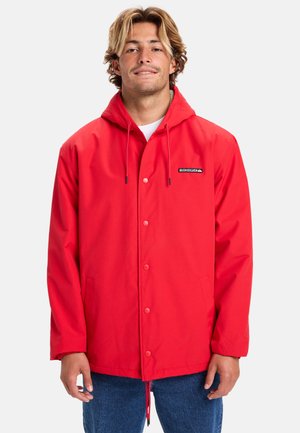 Rote wasserdichte Jacke mit Kapuze, vorne mit Druckknopfverschluss, Seitentaschen und einem Logopatch auf der Brust. Glatte Textur, lässige Passform.