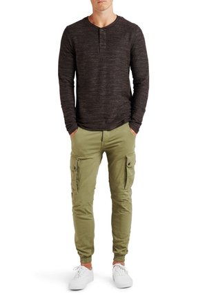 Černé henley tričko s dlouhým rukávem a texturovaným povrchem, doplněné olivově zelenými cargo kalhotami s bočními kapsami a elastickými manžetami. Bílé tenisky.
