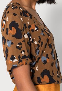 Haut brun à manches courtes avec un imprimé abstrait coloré en noir, blanc, orange et bleu, avec un col en V et une coupe ample.