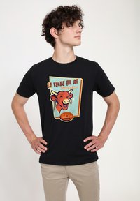 T-shirt in cotone nero con una grafica di una mucca sorridente con orecchini e la scritta "La Vache Qui Rit" in uno stile vintage colorato.