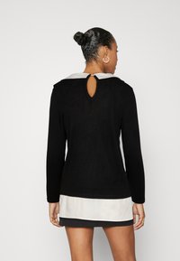 Pull noir à manches longues avec un col blanc et un détail en trou de serrure au dos. Présente une texture douce et un design à ourlet superposé.